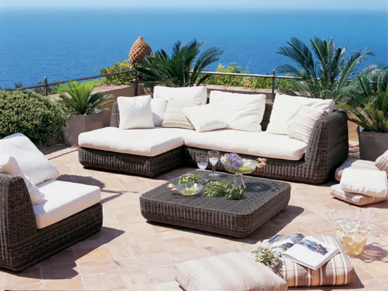divani e poltrona da esterno in fibra intrecciata marrone con cuscini panna su terrazza con vista mare, tavolino corredato, cuscini e palme