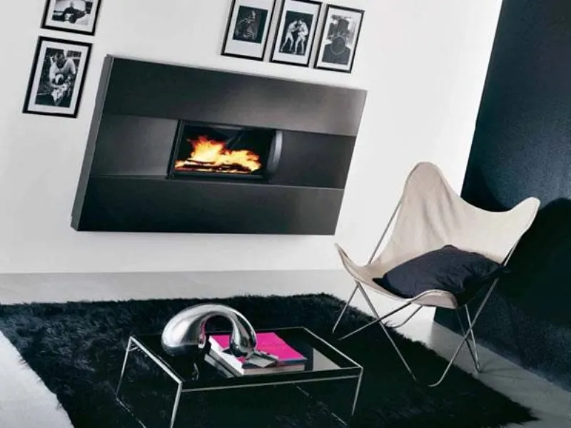 caminetto a parete con rivestimento nero acceso, seduta i tessuto panna, tappeto in pelo nero e tavolino con soprammobile design in acciaio