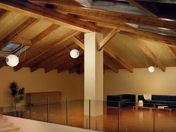 sottotetto con soffitto a travi e tre lampade a sfera bianche pendenti da soffitto con cavo