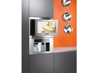 televisore incassato in mobile cucina grigio, tre pentole sospese a catena con parete di sfondo arancione