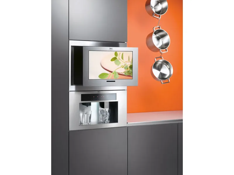 televisore incassato in mobile cucina grigio, tre pentole sospese a catena con parete di sfondo arancione