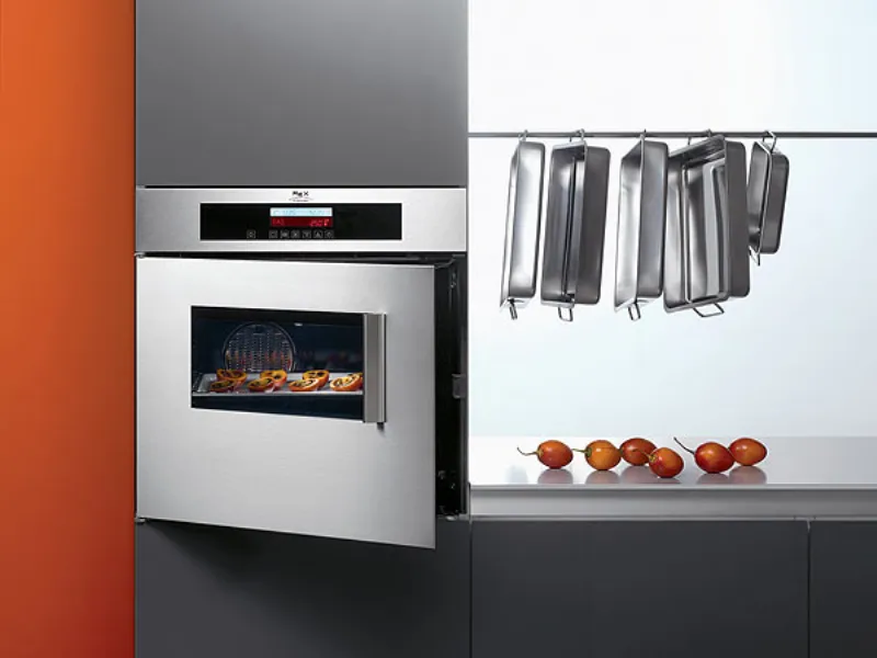 forno con apertura a libro incassato su mobile cucina tinta antracite, parete arancione sulla sinistra e teglie appese e pomodori sulla destra