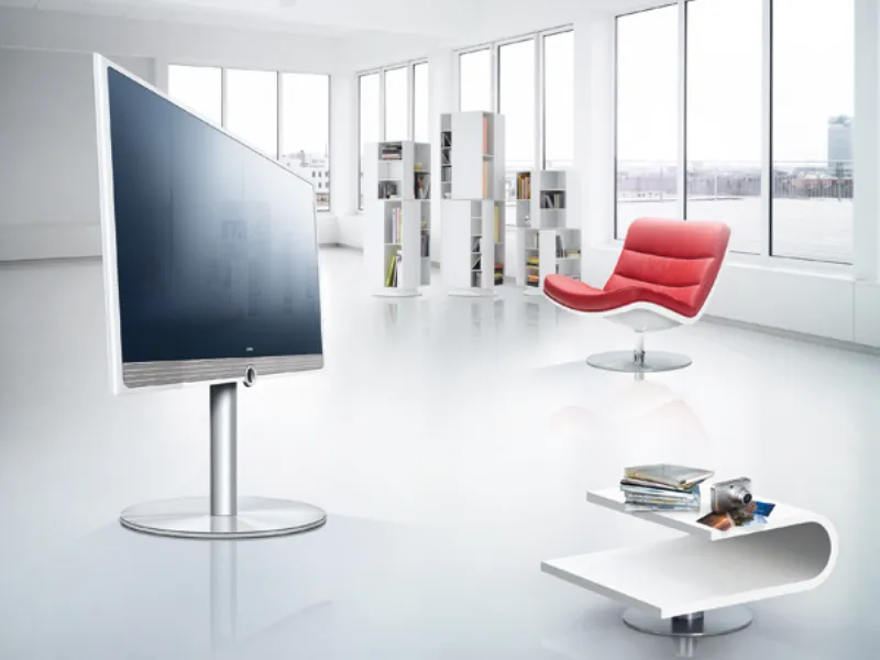 zona living bianca con seduta rossa e bianca, tavolino design e librerie bianche, schermo tv piatto e parete finestrata
