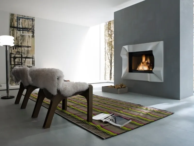 caminetto su parete grigia con cornice geometrica bianca, due poltrone in legno con rivestimento in pelo bianco, tappeto a fantasia a righe verde mela e pink